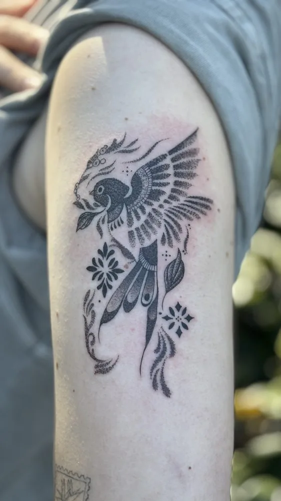 Black-and-grey dotwork bird in flight with decorative flowers tattoo