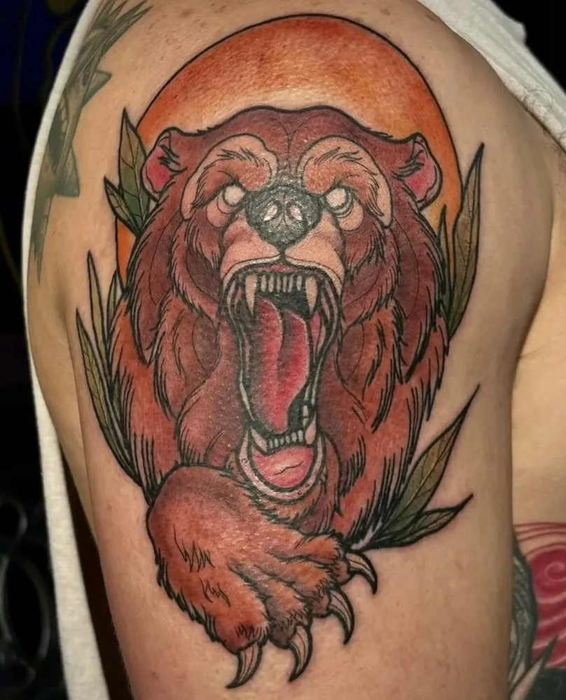 Neo-traditional roaring bear tattoo against an orange sun with foliage